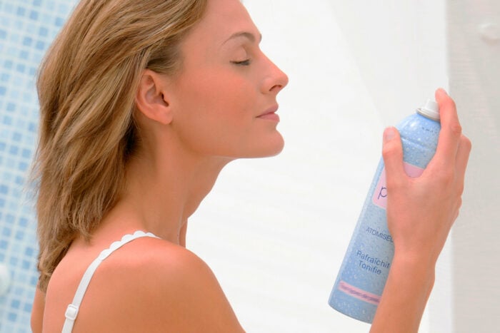 Jeune femme qui applique un brumisateur d'eau thermale sur son visage