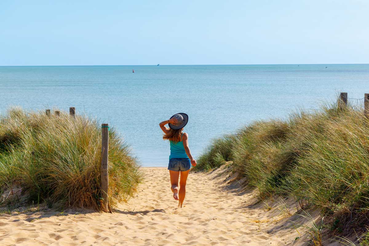 Jeune femme en mini-cure thermale dans les Landes marchant pied nus dans le sable face à l'océan
