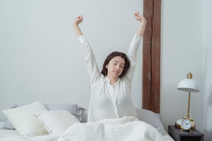 Jeune femme dans son lit en train de faire des étirements pour soulager un mal de dos au réveil © Pexels - Miriam Alonso