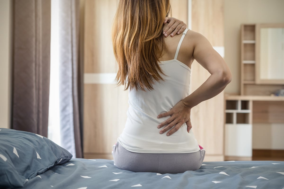 jeune femme assise sur un lit souffrant de mal de dos au réveil © AdobeStock