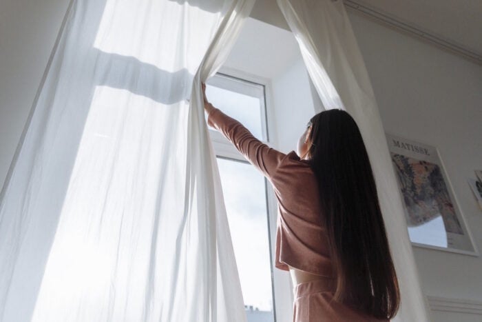 Femme ouvrant les rideaux pour s'exposer à la lumière naturelle et limiter les effets du changement d'heure sur le sommeil © Pexels - Thirdman