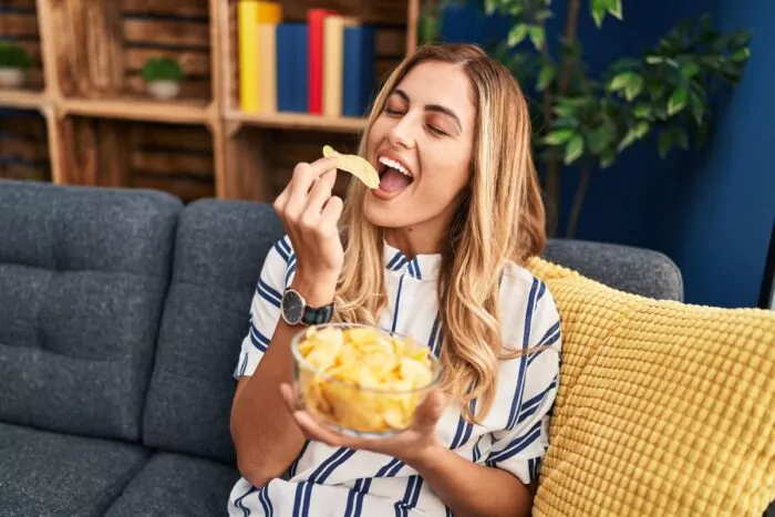 Jeune femme blonde mangeant des chips dans un canapé