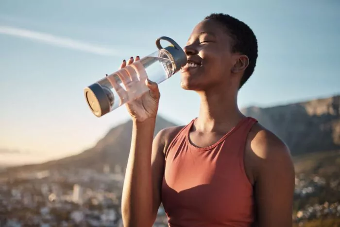 Jeune femme souriante en train de boire de l'eau pendant sa séance de sport