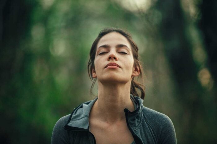 Femme de face en pleine nature qui ferme les yeux