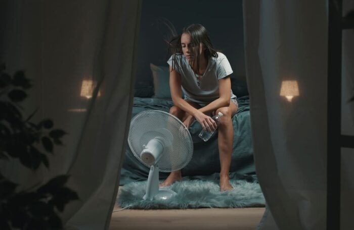 Femme dans sa chambre pendant la canicule, devant un ventilateur