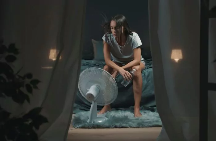Femme dans sa chambre pendant la canicule, devant un ventilateur 