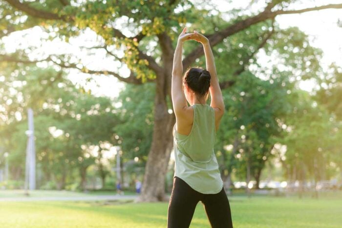 femme de dos qui s'étire dans un parc