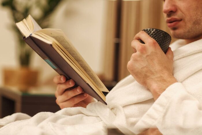 Jeune homme en peignoir avec une tasse à la main lisant un livre