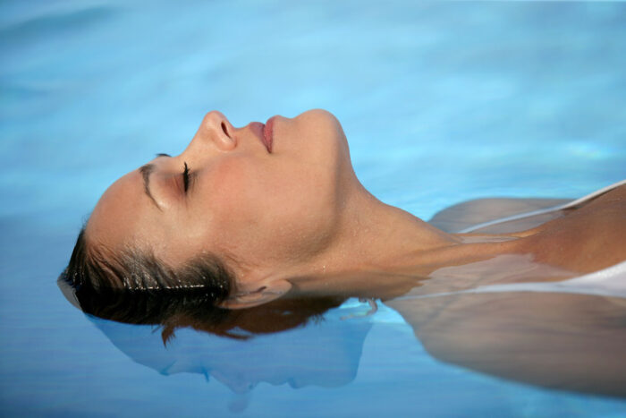 Femme qui flotte sur le dos les yeux fermés dans une piscine