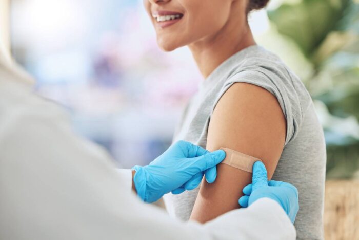 Femme souriante se faisant poser un pansement après avoir reçu une dose de vaccin