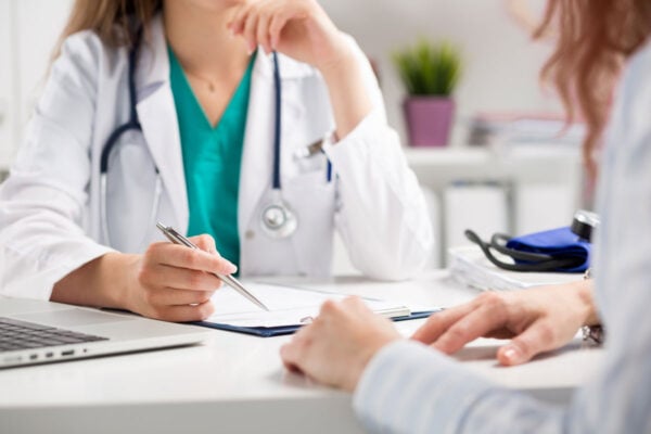 Patient en consultation face à un docteur tout deux assis de chaque côté d'un bureau