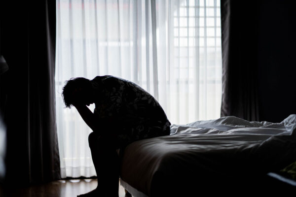 Homme assis sur le fond de son lit tenant la tête dans ses mains dans un état dépressif