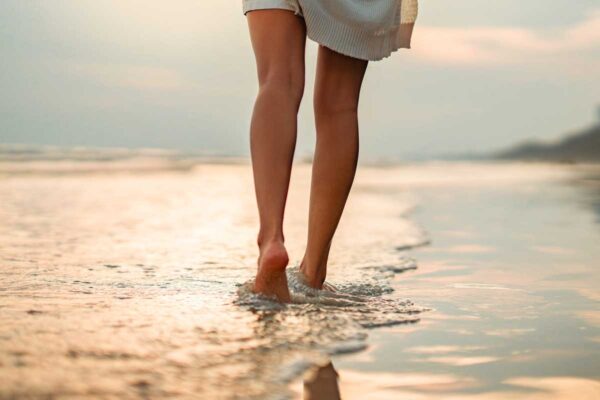 Jambe de dos d'une femme marchant pied nus sur une plage