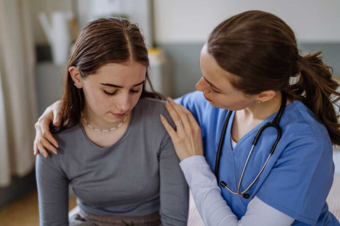 Une jeune fille assise à côté d'un docteur qui pose ses mains sur ses épaules pour la rassurer
