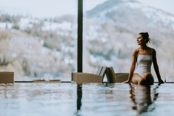 Femme assise au bord d'une piscine intérieure avec vu sur les montagnes enneigées