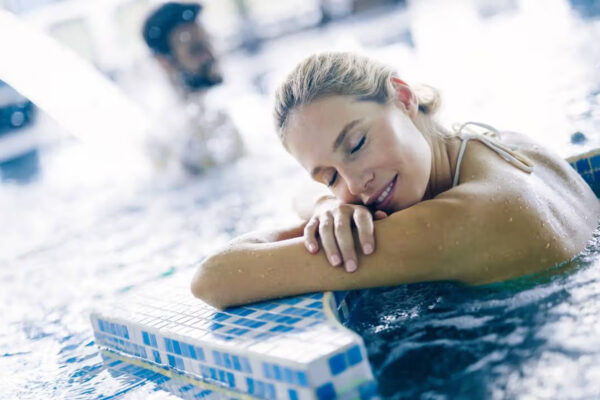 Jeune femme dans l'eau, la tête allongée sur ses bras croisé appuyée sur le bord d'une piscine
