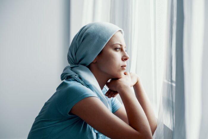 Jeune femme avec un foulard bleu suggérant la maladie et regardant au loin par une fenêtre
