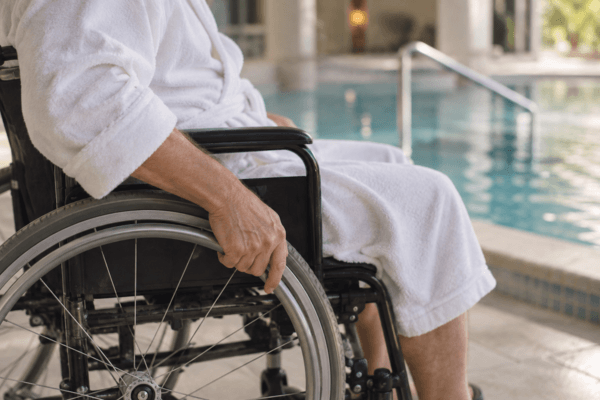 Curiste en peignoir assis dans un fauteuil roulant au bord d'une piscine lors d'une cure thermale PMR