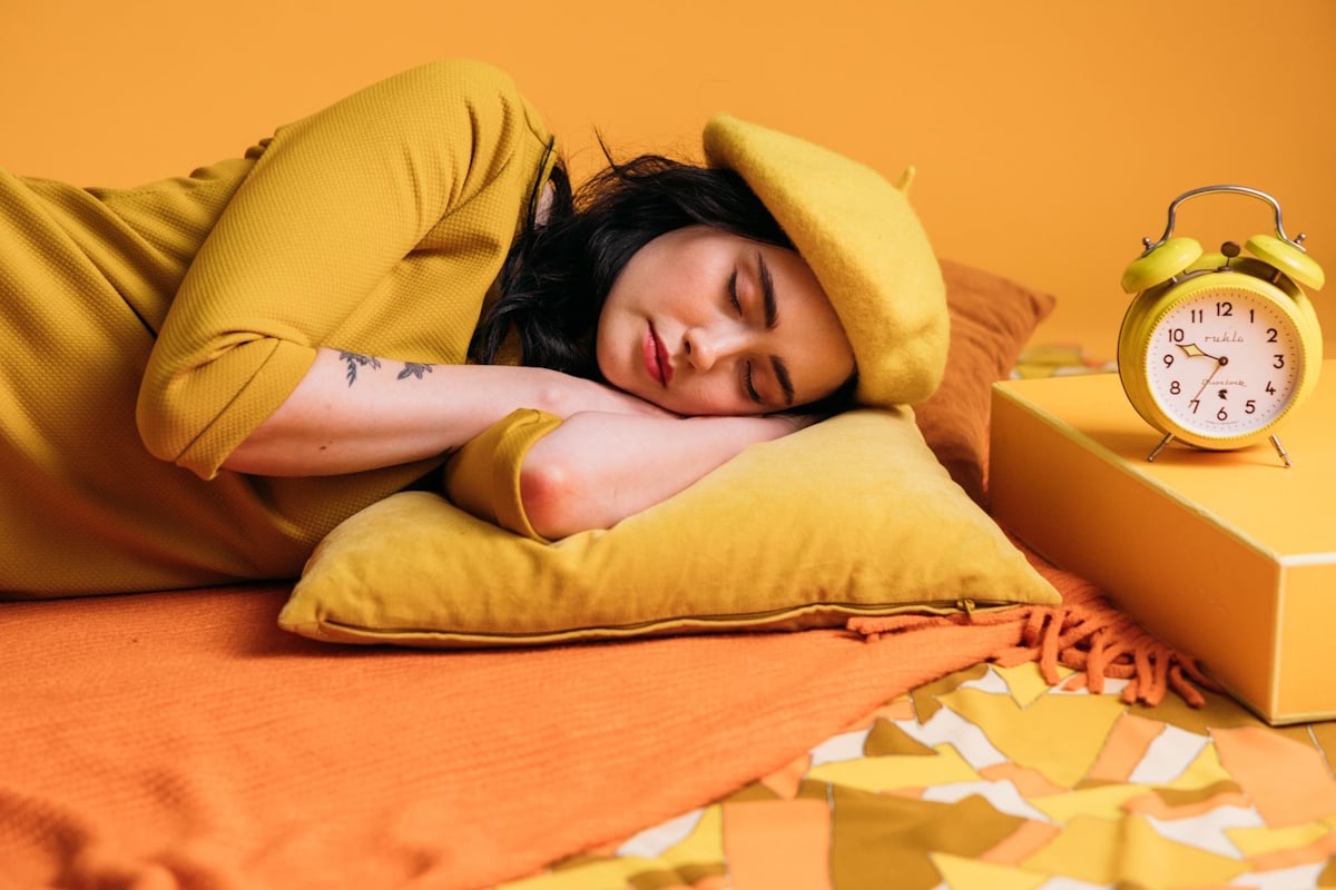 Femme endormie près d'un réveil jaune, pour illustrer les effets du changement d'heure sur le sommeil © Pexels - KoolShooters